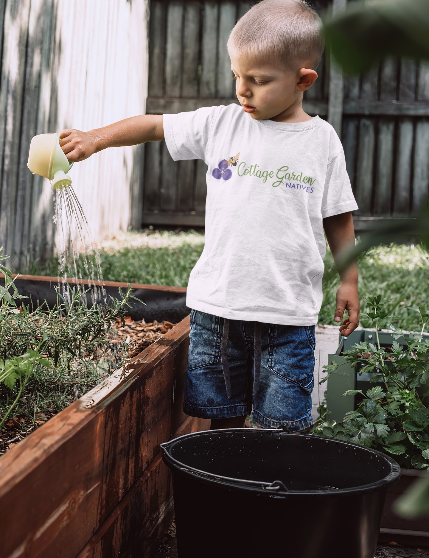 A custom logo design for Cottage Garden Natives with a bee and flower icon shown on a t-shirt worn by a child watering plants in a garden